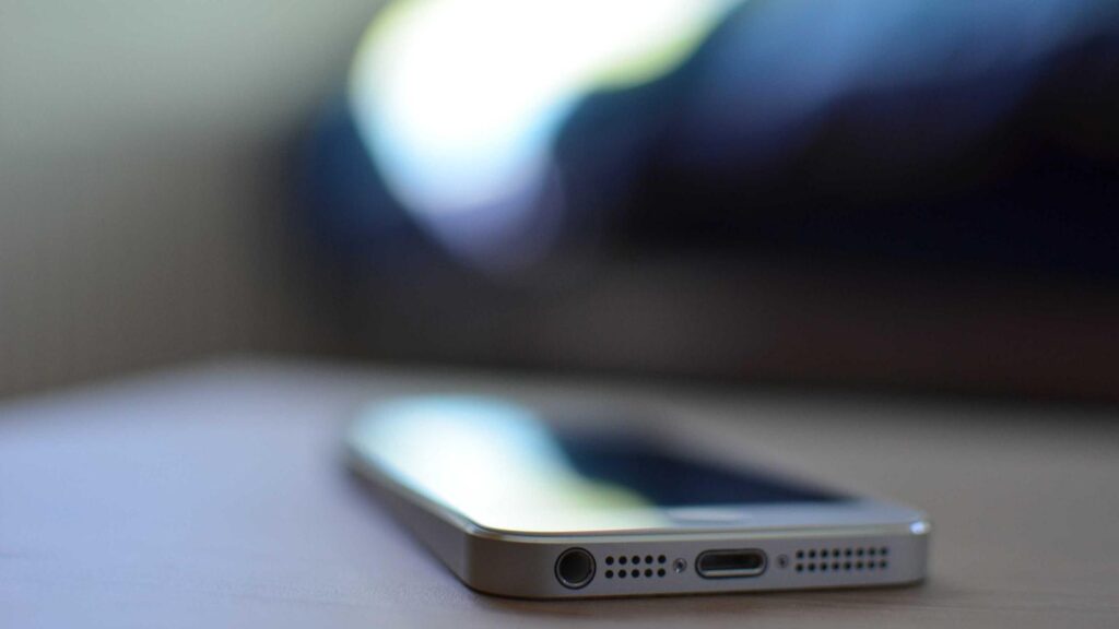 An iPhone on a wooden desk next to a notebook, pen, and coffee