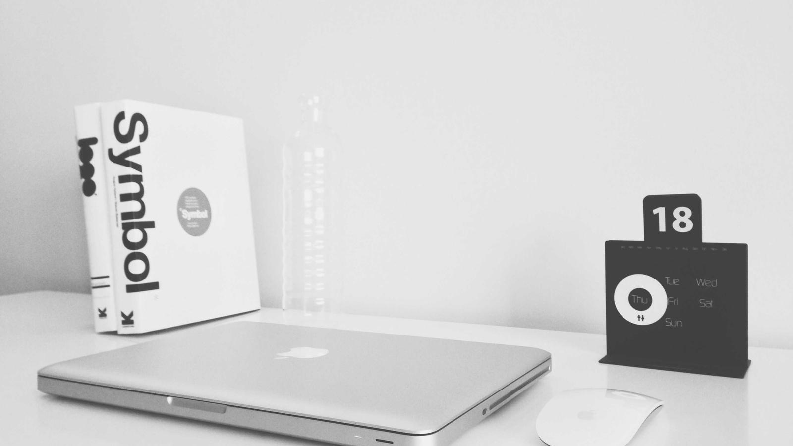 Apple MacBook Pro workspace with Magic Mouse, calendar, books, and potted plant