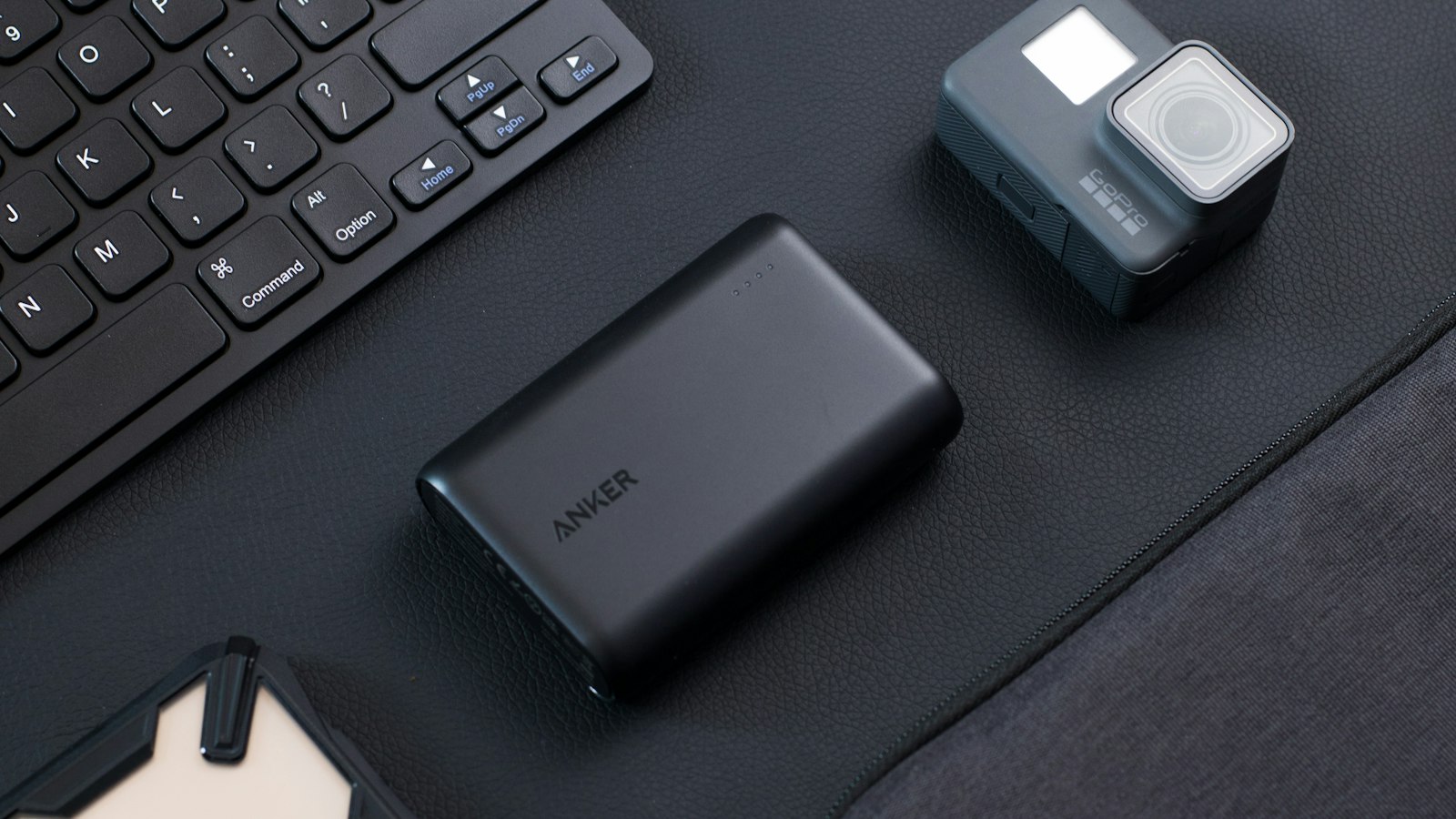 Portable Anker power bank beside a keyboard and smartphone on a dark desk